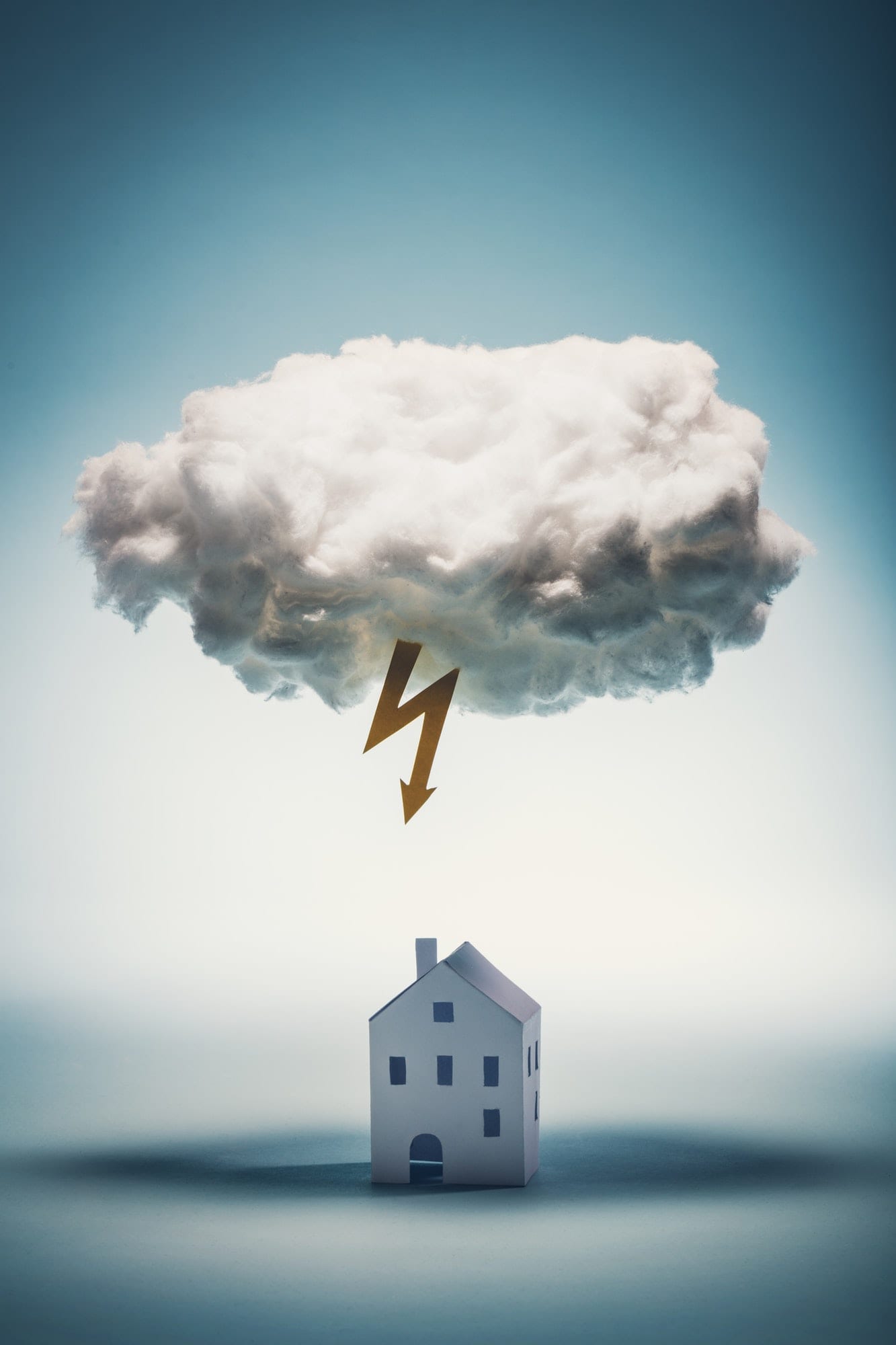Paper house standing under a white cloud with yellow lightning